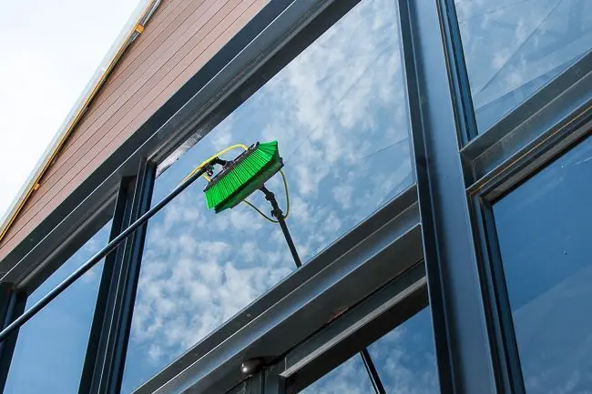 A water-fed pole brush cleaning the exterior glass windows of a modern residential home exterior in Greenville, Wisconsin.